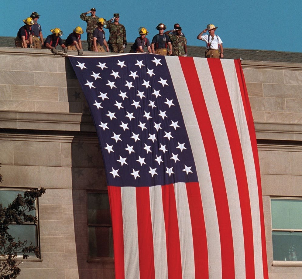 Firefighters unfurl a large American flag over the scarred stone of the Pentagon on September 12, 2001. White House photo by Paul Morse.